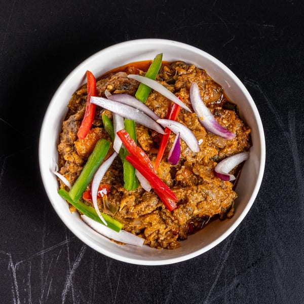 A bowl of American stew, garnished with red and green bell peppers and sliced white and red onions.