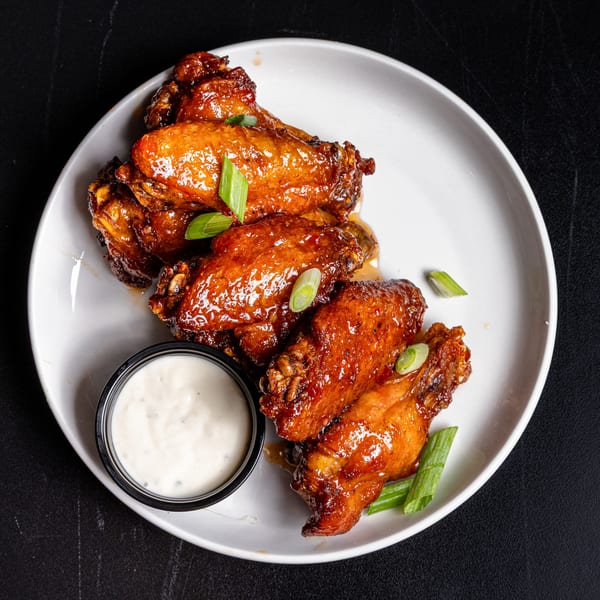 Glazed chicken wings with sliced green onions and a side of ranch dressing on a white plate.