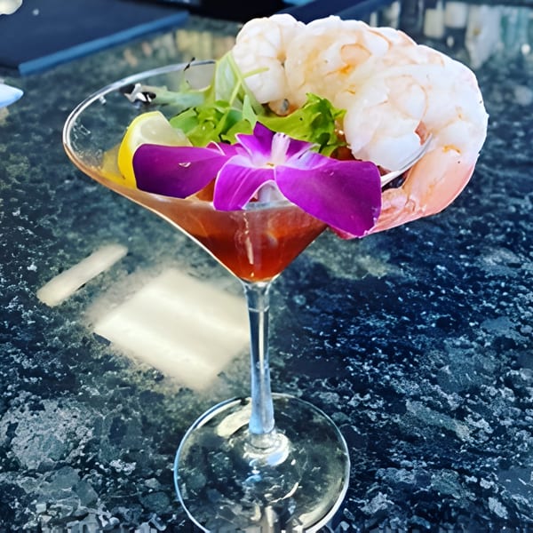 Shrimp cocktail in a martini glass with lemon, greens, and a purple orchid garnish.