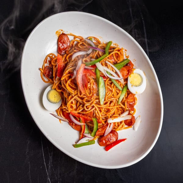 Steaming spaghetti with sausage, bell peppers, onions, and hard-boiled eggs on a white plate.