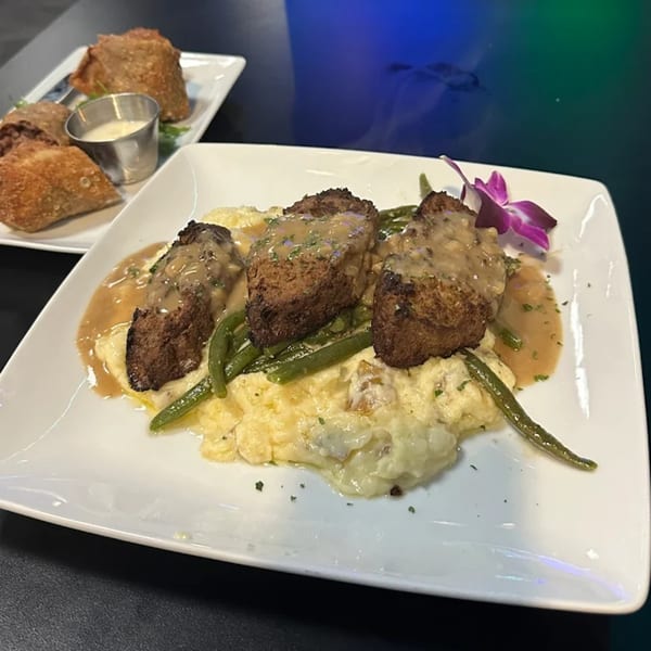 Meatloaf with gravy, mashed potatoes, and green beans, garnished with an orchid, and egg rolls.